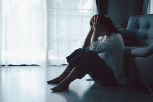 Tired depressed desperate tired girl sadly sitting on couch at home. Young woman is sitting on floor living room, feeling sad and depressed. Psychological problem. Depression and loneliness concept.