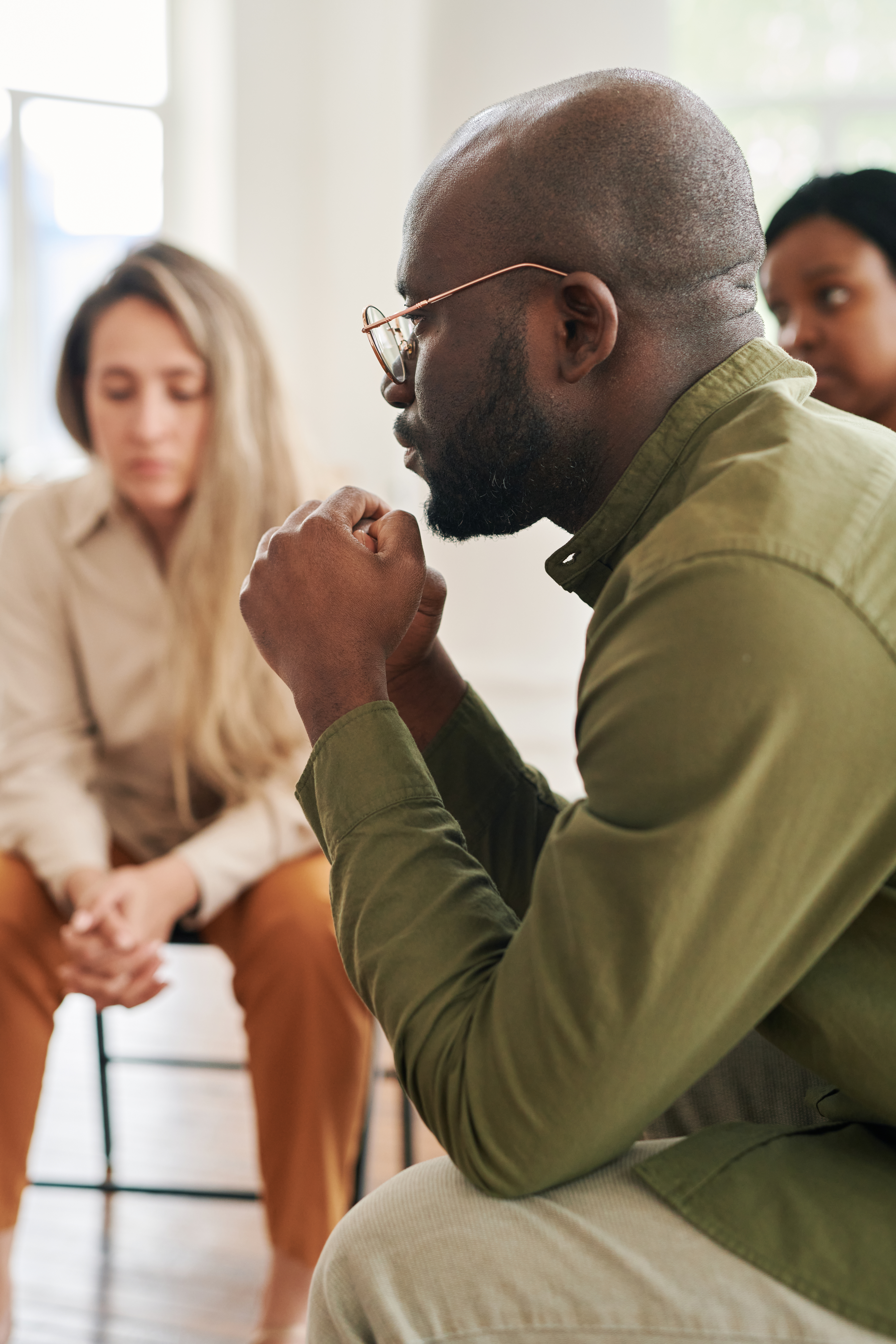 Side view of young stressed man with interlocked hands by his face sharing his problem while attending psychological session