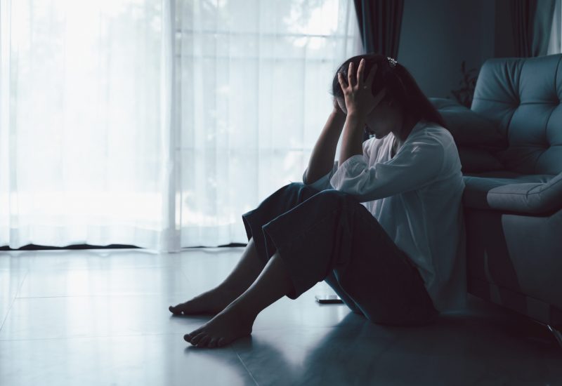 Tired depressed desperate tired girl sadly sitting on couch at home. Young woman is sitting on floor living room, feeling sad and depressed. Psychological problem. Depression and loneliness concept.